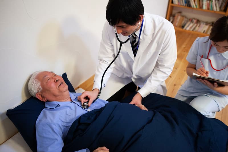 A doctor on call treating an elderly patient in his NYC home.